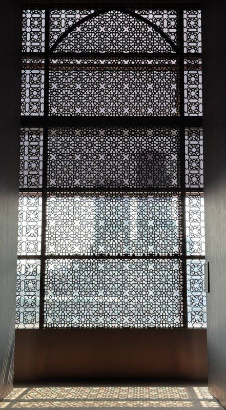 Light pouring through a carved lattice screen in a dark gallery
