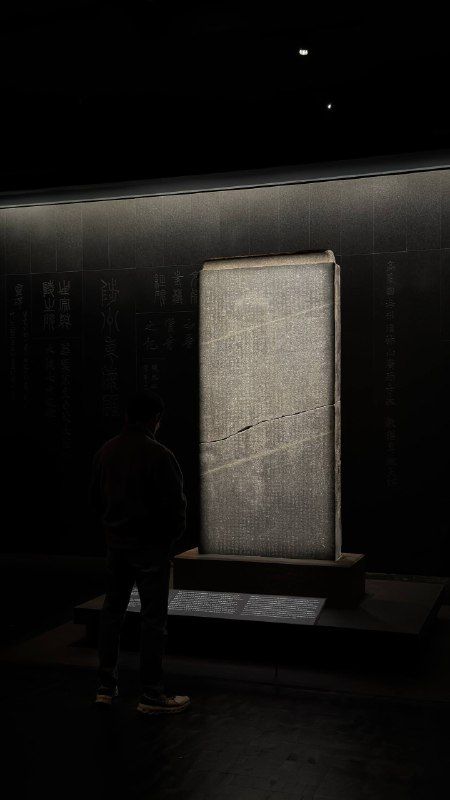 A pale stone stele standing alone in a dark gallery