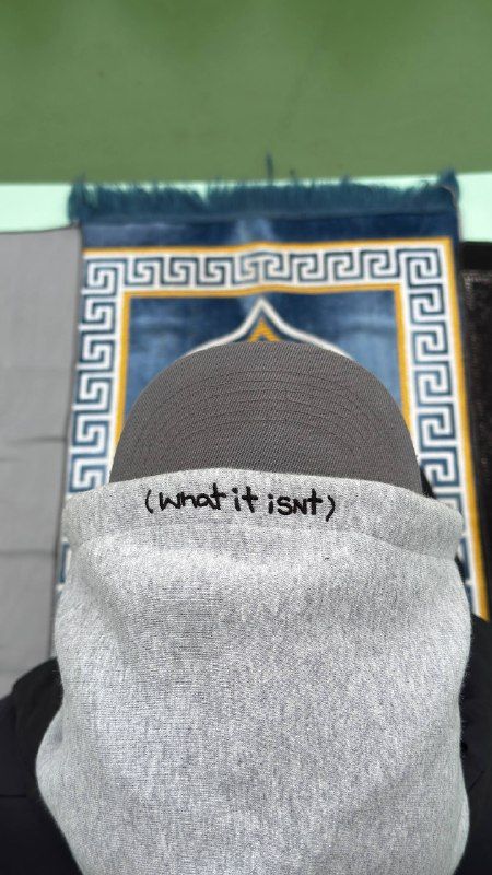A prayer-mat print behind a grey sock with "what it isn’t" stitched on it