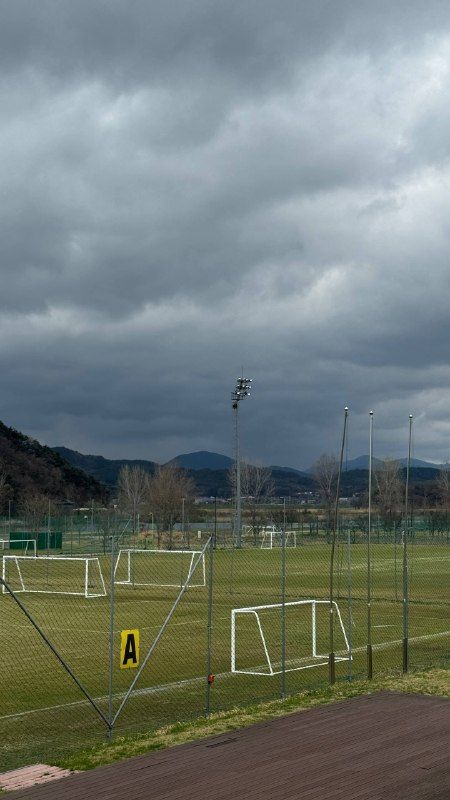 A football pitch with goals under heavy grey clouds and mountains