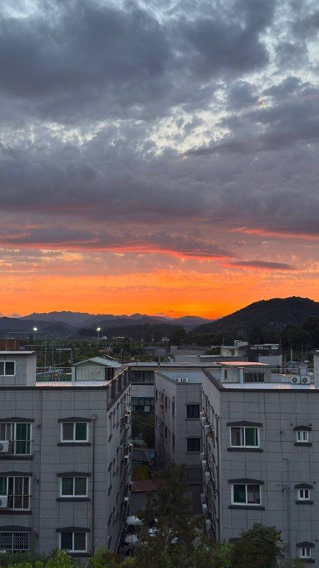 An orange sunset band beneath dark clouds over apartment rooftops