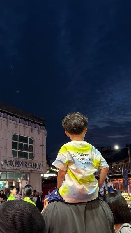 A boy on his father's shoulders at a night street festival