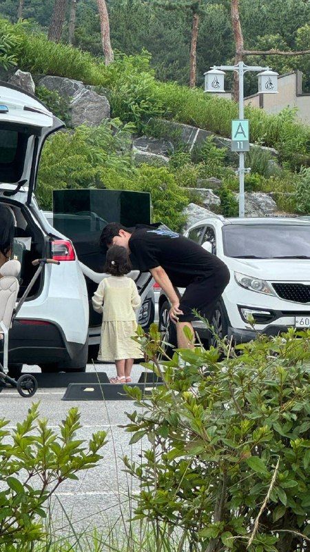 A small girl beside an open car boot in a hillside car park