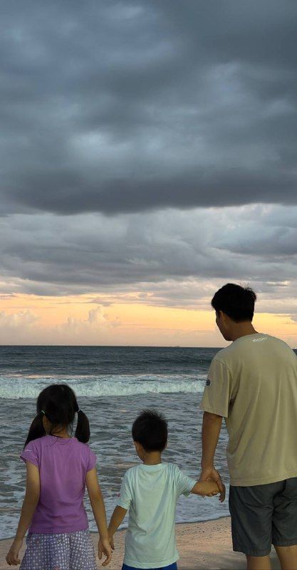 A father and two children holding hands at the shore under storm clouds
