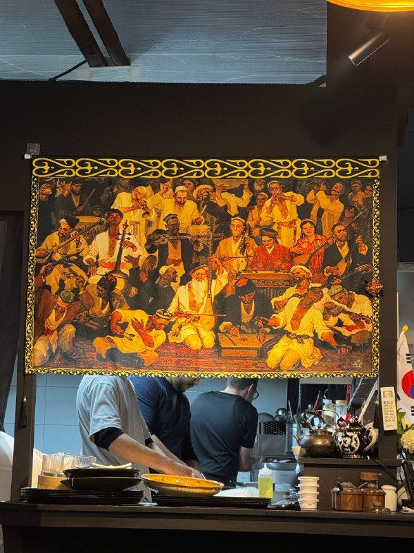 An open kitchen under a large gilded painting of a feast