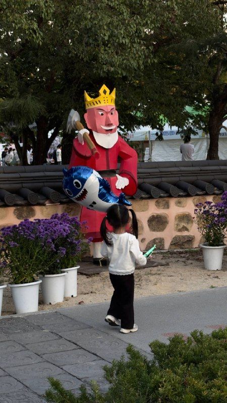 A costumed king performer and a small girl in a festival courtyard