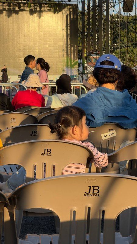 Children and parents in rows of folding chairs at an outdoor show