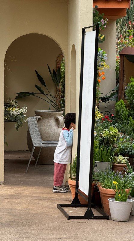A child looking into a tall mirror in a plant-filled arcade