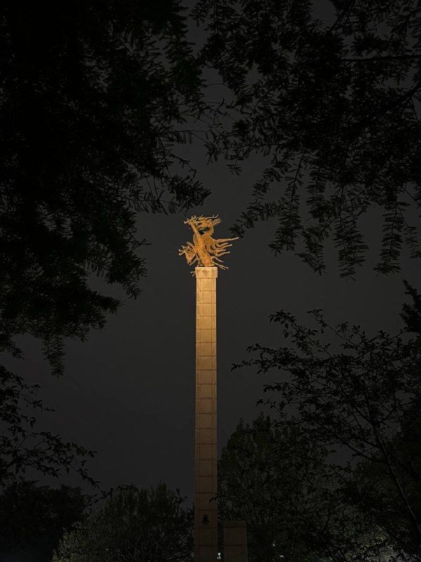 A lit stone column glowing in a dark park at night
