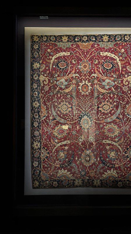 A red medallion carpet hanging in a museum gallery